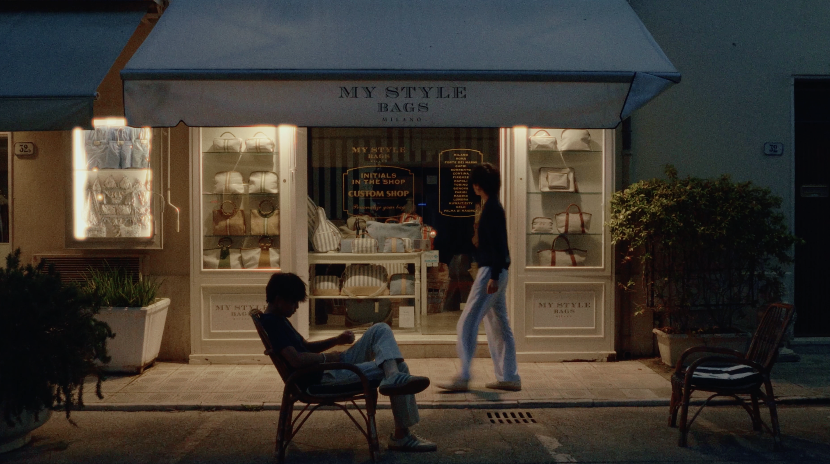 Two people outside a warmly lit shop in Europe at night